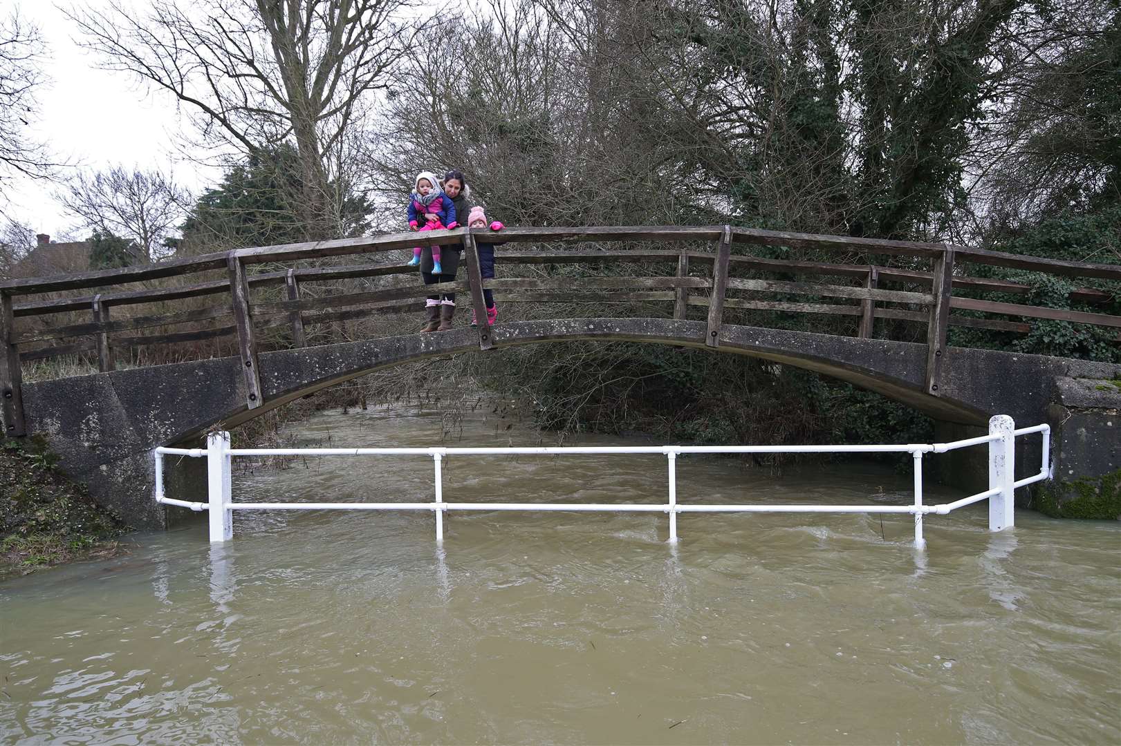 People cross a bridge over a swollen River Chelmer in the village of Great Easton, Dunmow, where it burst its banks (Yui Mok/PA)