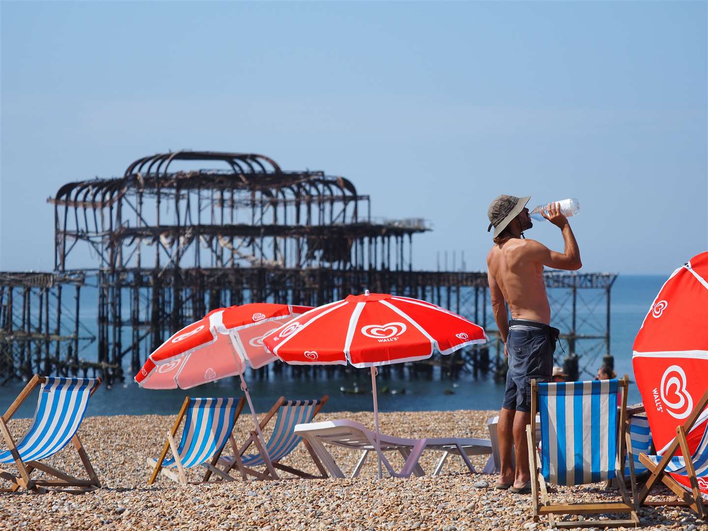A man takes a drink of water besides deckchairs and beach umbrellas on Brighton beach (Joe Sene/PA)