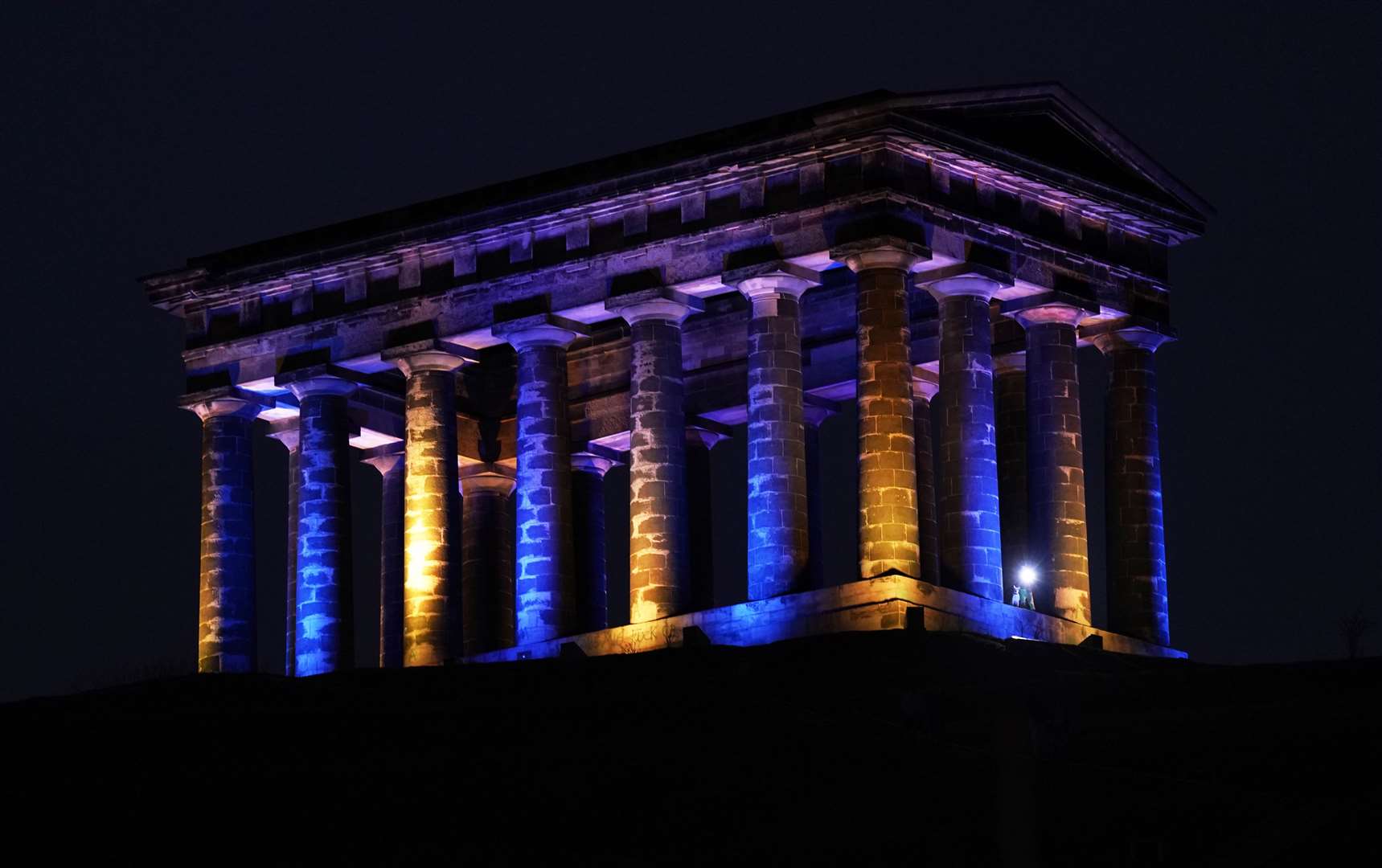 The Penshaw Monument near Sunderland flooded with blue and yellow lights during the night to mark the one-year anniversary of the start of the conflict (Owen Humphreys/PA)
