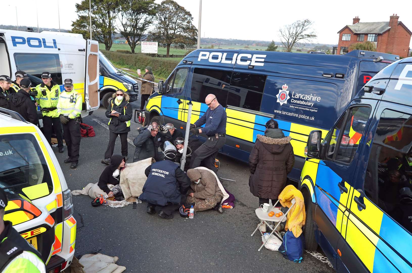 A police team cuts a man and woman out of a set of tyres, which they had apparently cemented their arms into, outside energy firm Cuadrilla’s site in Preston New Road (PA)