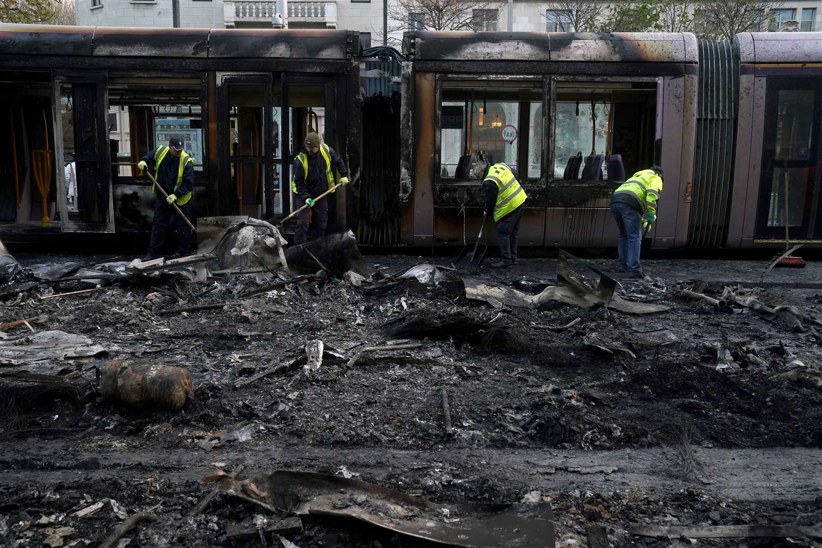 Debris is cleared from a burned out Luas and bus on O’Connell Street in Dublin (Brian Lawless/PA)