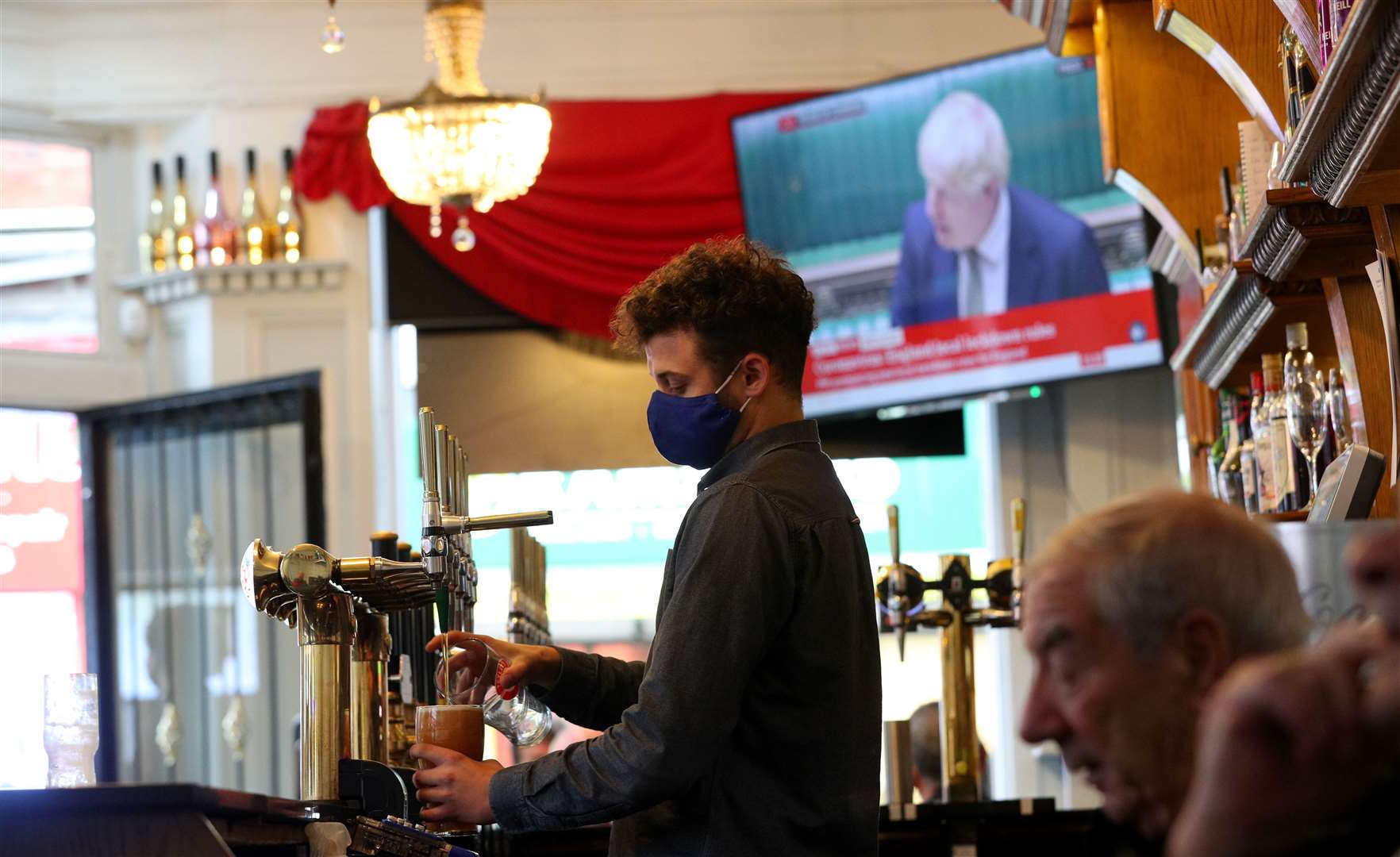 A member of staff pours a drink in the Richmond pub in Liverpool as Prime Minister Boris Johnson reads a statement on television (Peter Byrne/PA)