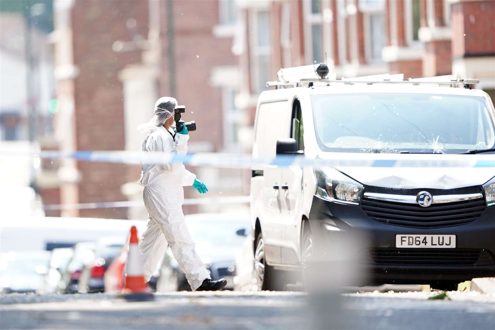 A police forensics officer photographs a white van on the corner of Maples Street and Bentinck Road (Zac Goodwin/PA)