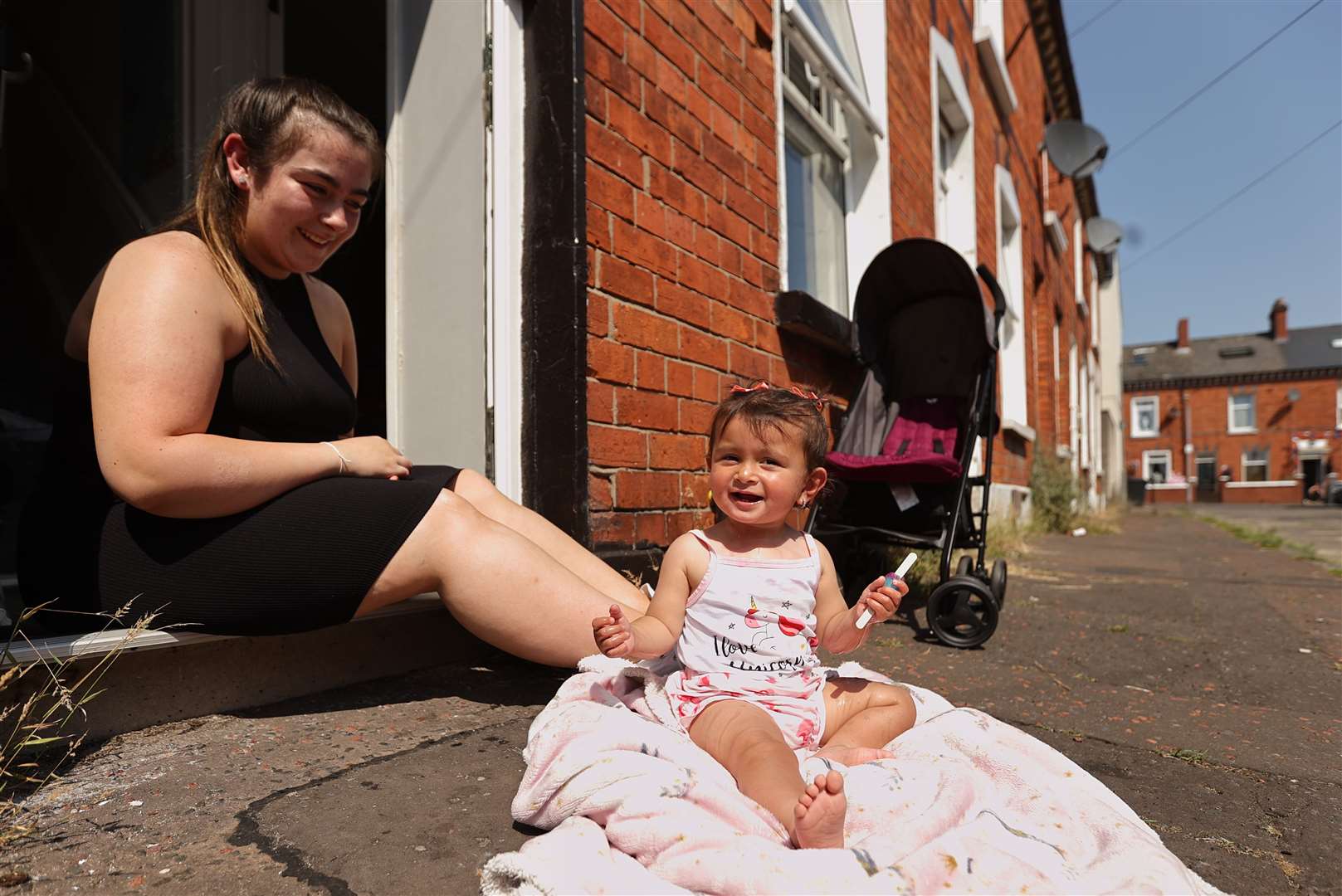 Jasmine Bowers with her daughter Harmony aged one eating a lollipop and enjoying the hot weather outside their home off the Shankill Rd in north Belfast (Liam McBurney/PA)