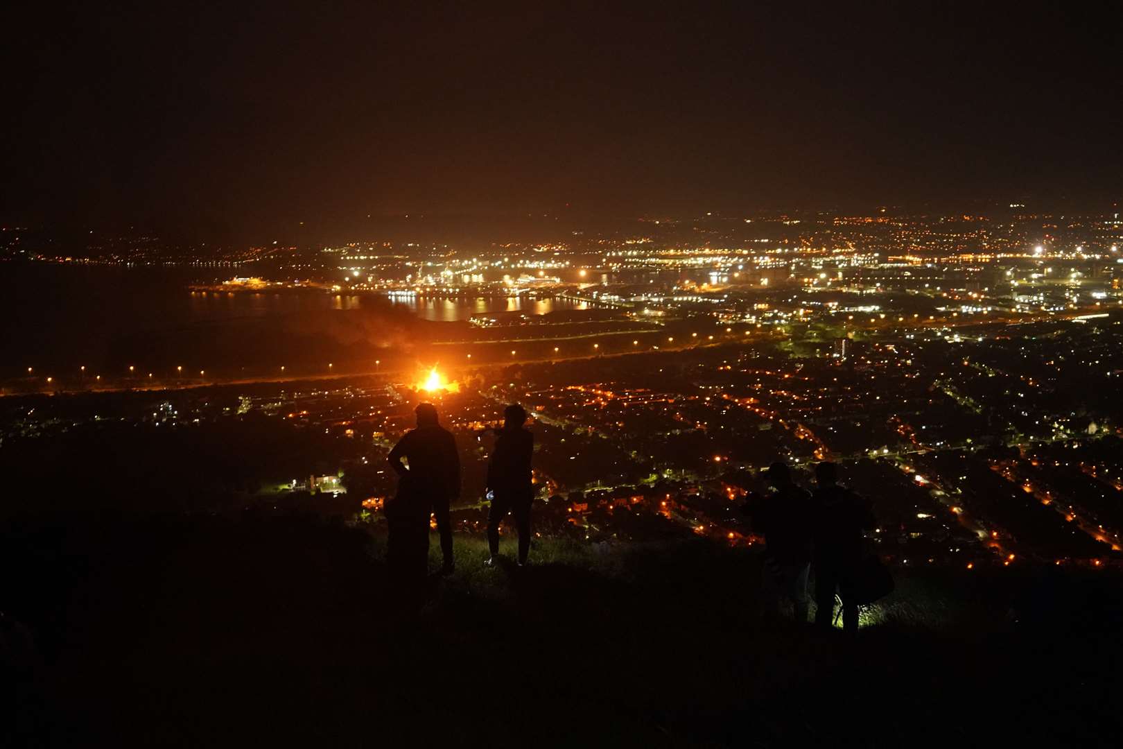 People stand on Cavehill in Belfast as they watch bonfires being lit across the city on the ‘Eleventh night’ to usher in the Twelfth commemorations (Niall Carson/PA)
