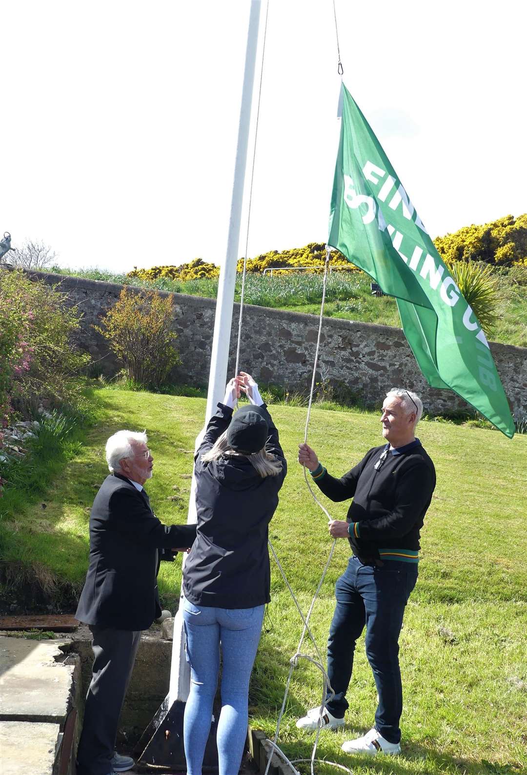 Club president Jim Gardner assists Vanessa and Ian Ramsay in unfurling the Findochty flag. Photo: Peter MacDonald