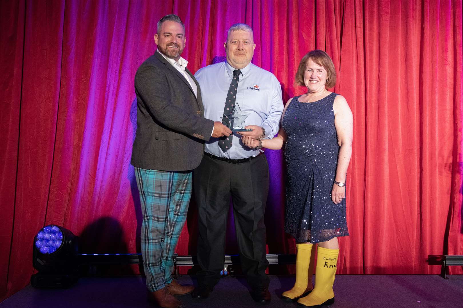 Buckie RNLI coxswain Davie Grant (centre) and LOM Anne Scott – complete with a pair of yellow wellies – accept the Emergency Services trophy from Dave Acton, CEO of Motive Offshore. Picture: Beth Taylor.