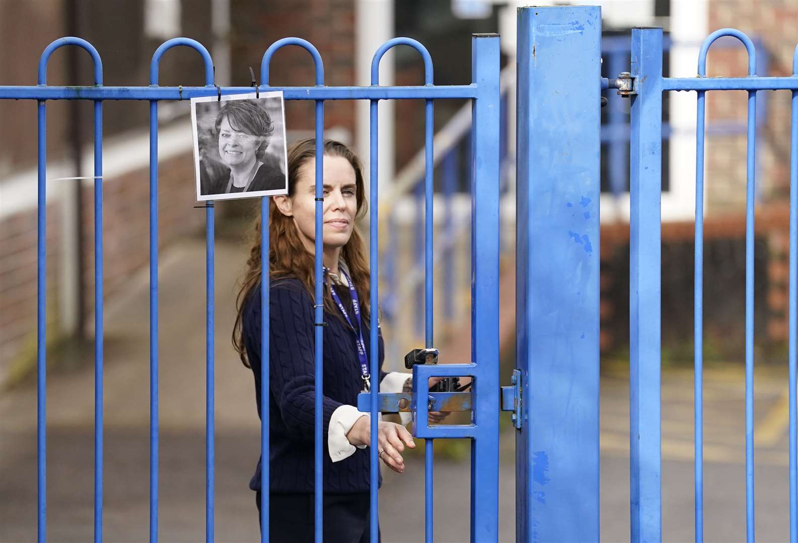 Headteacher Flora Cooper, wearing a black armband, stands next to a photograph of Ruth Perry as she closes the school gate at John Rankin Schools in Newbury, Berkshire (Andrew Matthews/PA)