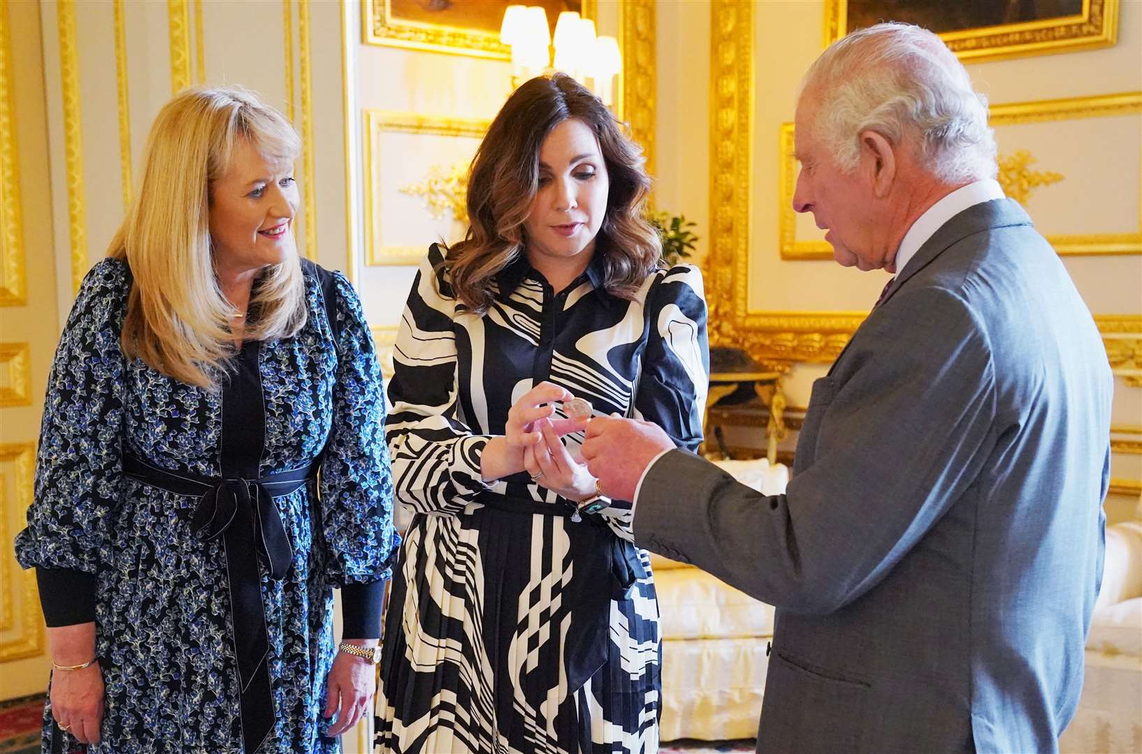 The King is presented with the first struck £5 coronation coin by Royal Mint chief executive Anne Jessopp and director Rebecca Morgan at Windsor Castle (Jonathan Brady/PA)