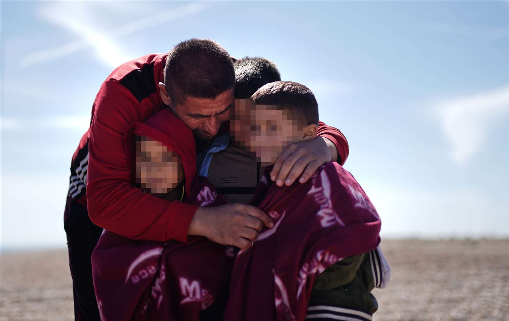 A man and children, thought to be asylum seekers, embrace after arriving in Dungeness (Jordan Pettitt/PA)