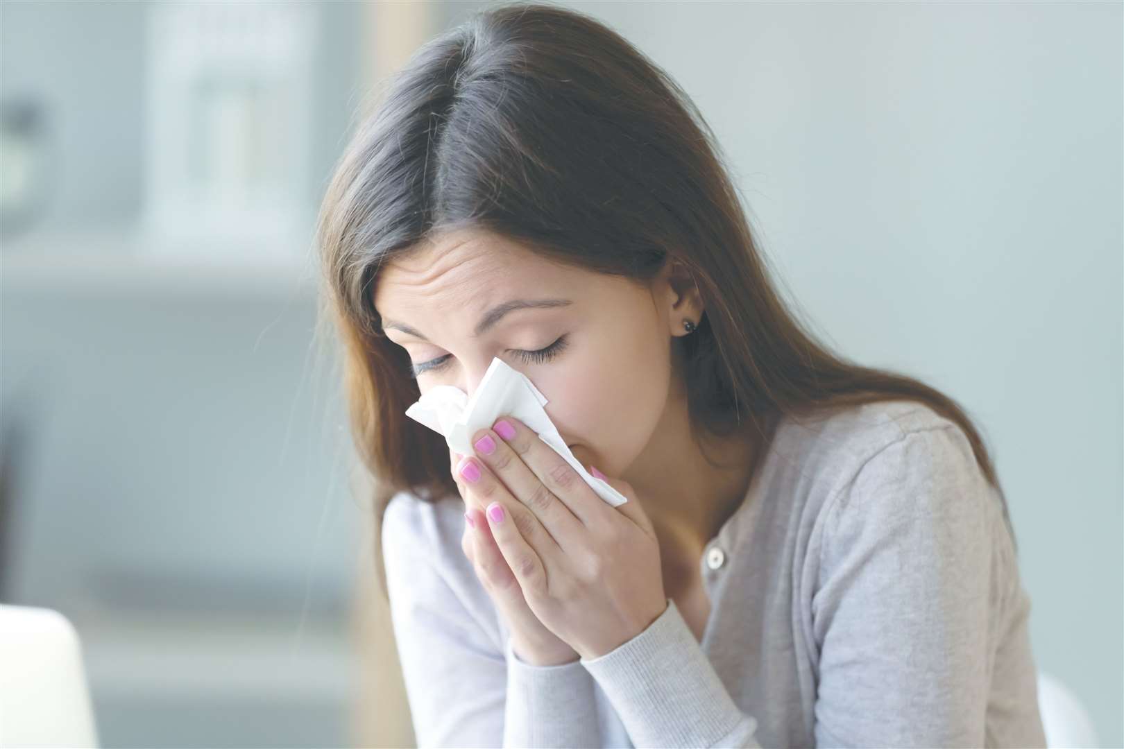 Sick young woman sitting indoors holding tissue handkerchief blowing running nose feels unwell unhealthy, girl having symptoms of chronic sinusitis disease, seasonal allergy or cold fever flu concept