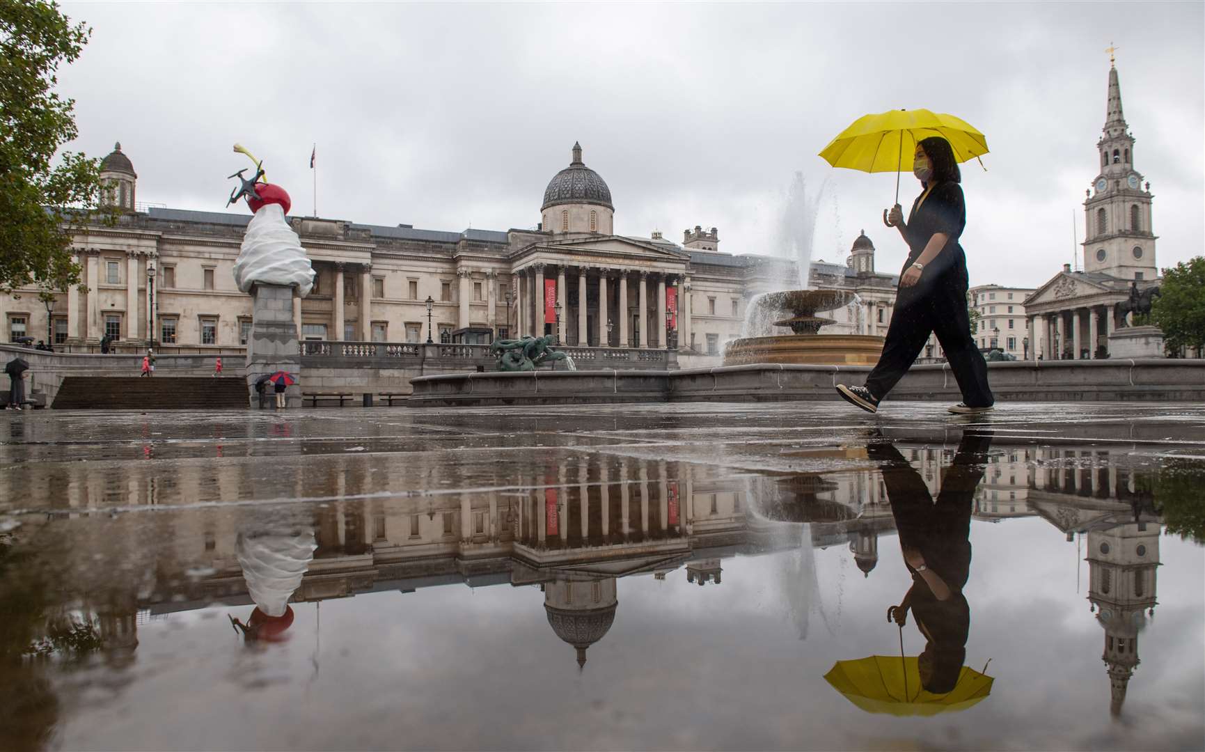 A woman shelters from the rain under an umbrella as she walks through Trafalgar Square, London (Dominic Lipinski/PA)