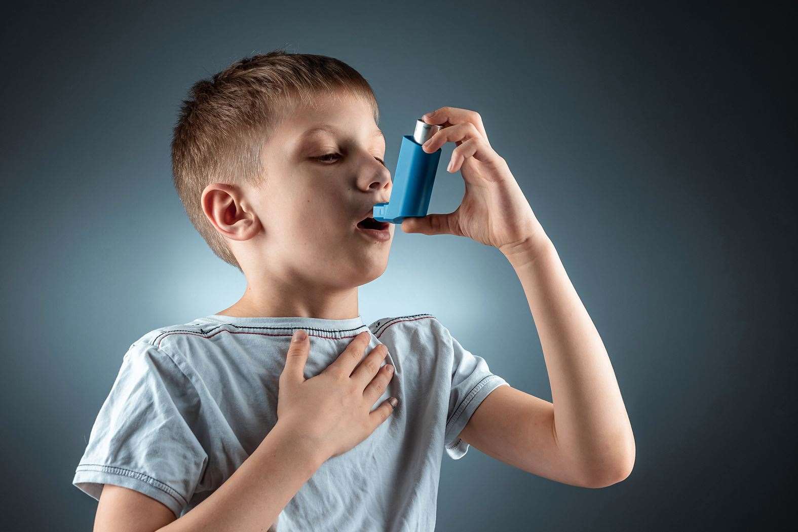 A young boy uses his blue inhaler to get relief from asthma.