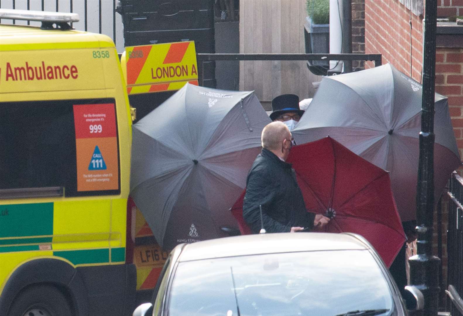Staff shield the exit with umbrellas alongside an ambulance outside the rear of the King Edward VII Hospital (Dominic Lipinski/PA)